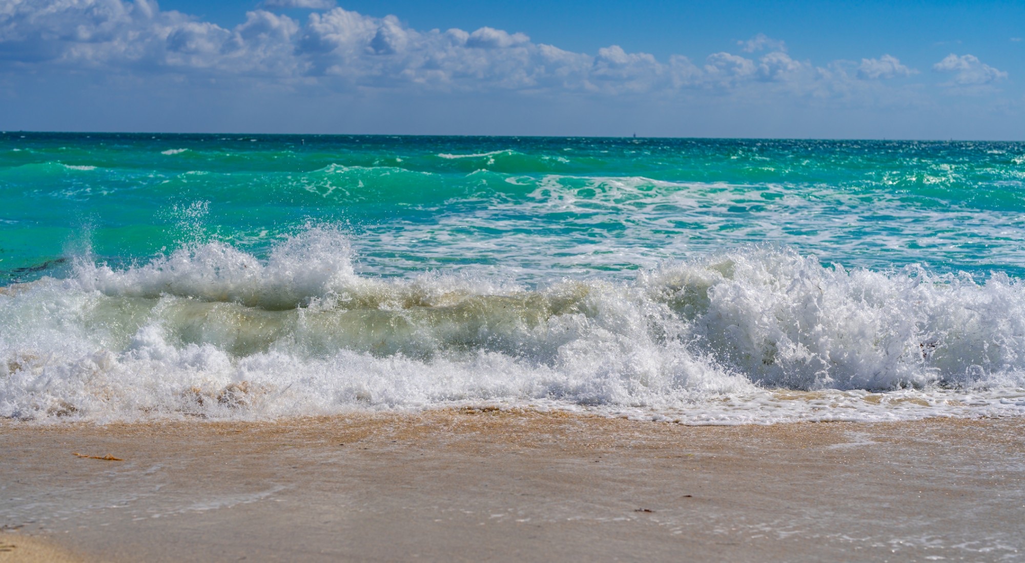 Waves breaking on a sandy beach under a blue sky